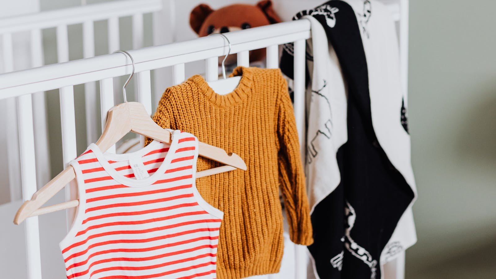 Vêtements de bébé sur des cintres en bois suspendus devant un lit à barreaux blanc