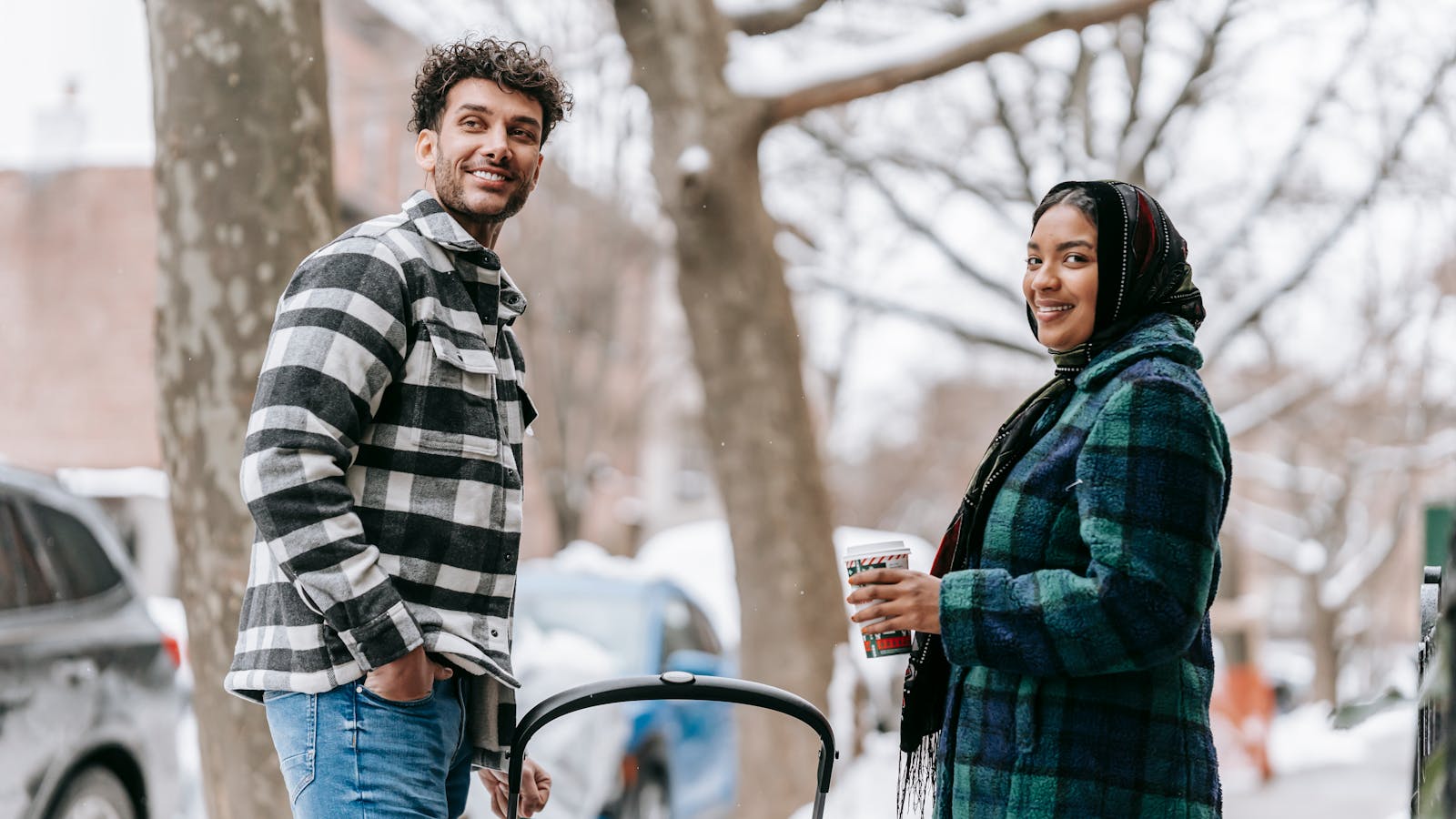 Couple souriant en ville à côté d'une poussette, tenant un café